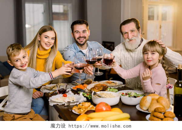 家族晚餐聚会家庭共进晚餐庆祝概念，感恩节假期。 一家人幸福地坐在桌旁笑着，享受着在一起的时光，享用着美味的晚餐，手里拿着酒杯和果汁